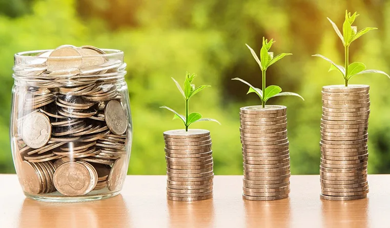 Pièces de monnaie dans un bocal et pousses vertes symbolisant les économies